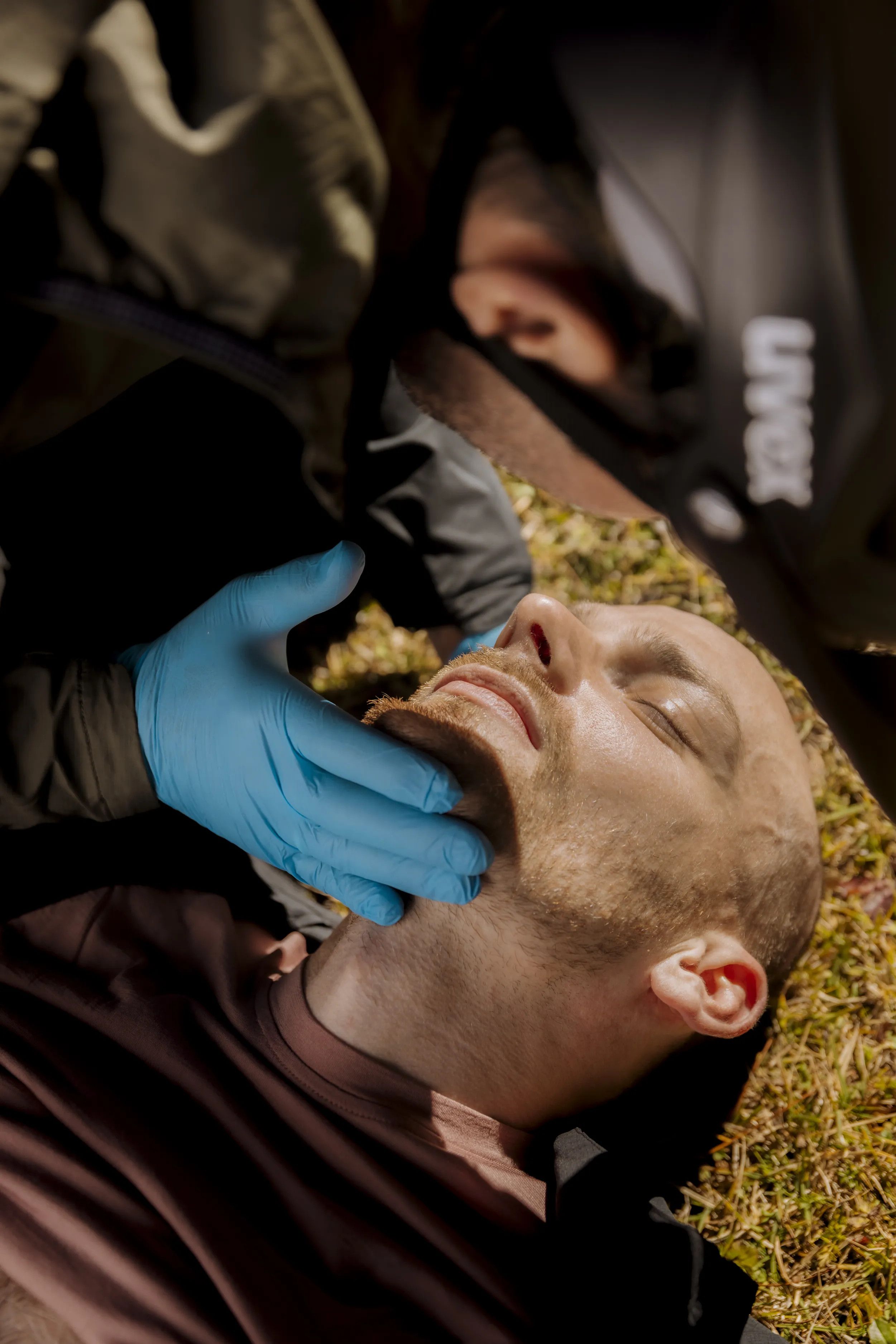 gloved hand, medical exam, facial touch, lie down, outdoor scene